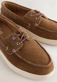 Braune Wildleder-Bootsschuhe mit weißen Nähten, Schnürdesign und beigen Akzenten. Runde Zehenform und Gummisohle mit strukturiertem Grip.