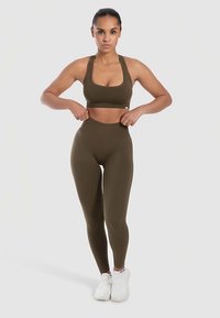 Oliivinvihreä urheiluliivit ja legginsit, jotka on valmistettu sileästä, joustavasta kankaasta. Kangas on vartaloa myötäilevä, korkean vyötärönauhalla ja racerback-mallisella selkäosalla.