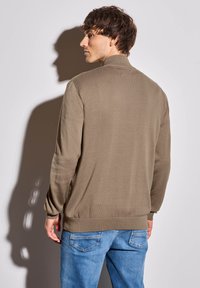 Hnědý lehký svetr s vysokým límcem, ribovanými manžetami a lemem, spojený s světle modrými džínami. Hladká struktura, minimalistický design.