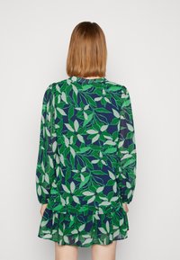 Groene en marineblauwe bloemenjurk met lange mouwen, plooidetail bij de halslijn en een gerimpelde zoom. Gemaakt van lichtgewicht, vloeiende stof.