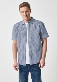 Košile s krátkým rukávem z modro-bílého vzorovaného materiálu, s límcem a rovnými lemy, nošená přes bílý tričko.