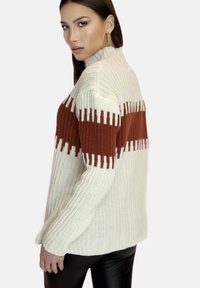 Stickad tröja med hög halsdesign, krämfärgad kropp med rostfärgade horisontella ränder, ribbad textur och avslappnad passform på ärmarna.