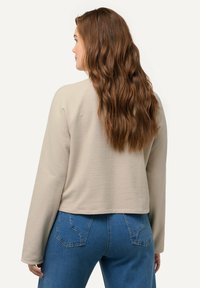 Beige cropped sweatshirt met lange mouwen, zachte textuur en ronde hals, gecombineerd met blauwe slim-fit jeans met achterzakken.