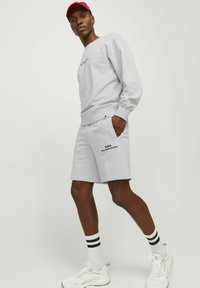 Gray sweatshirt and shorts set, featuring a crew neck, ribbed cuffs, and logo detail on shorts. Model wears red cap and white sneakers.