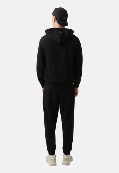 Schwarzer Kapuzenpullover mit einem schlichten Design und gerippten Bündchen, kombiniert mit schwarzen Jogginghosen. Das Outfit wird mit einer schwarzen Mütze abgerundet.