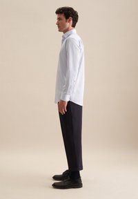 Camicia button-up a righe azzurre, maniche lunghe, con un orlo leggermente curvato, abbinata a pantaloni blu scuri e scarpe nere.