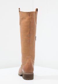 Botte en cuir marron hauteur genoux avec un bout rond, surface texturée, fermeture éclair sur le côté et un talon bas. Détails cousus sur les coutures.