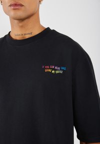 Svart bomull T-skjorte med korte ermer. Har flerfarget brodert tekst: "HVIS DU KAN LÆSE DETTE, TA MED KAFFE TIL MEG." Enkelt design.