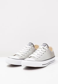 Grey canvas sneakers with white laces, rubber soles, and black trim. Features a textured upper with a logo tag near the tongue.