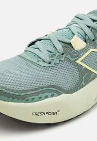 Mesh running shoe in light blue, featuring a textured upper, padded tongue, laces, and branding on the sole. Accented with green details.