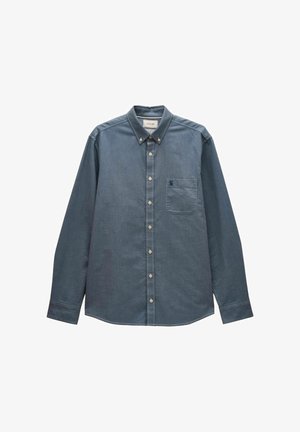 Mann krempelt den Ärmel eines hellblauen Hemdes mit Knöpfen hoch, zeigt die weiße Innenseite der Manschette und ein kleines Stoffetikett.