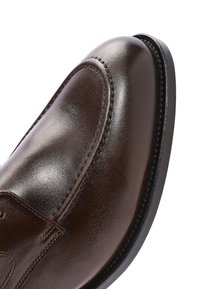 Close-up van een donkerbruine, gepolijste leren nette schoen met ronde neus en gedetailleerd stiksel langs de bovenkant en de randen van de zool.