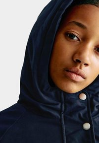 Námořnická kapucí bunda s hladkou texturou, s zipem a cvoky, a s prošíváním kolem obličeje a krku.