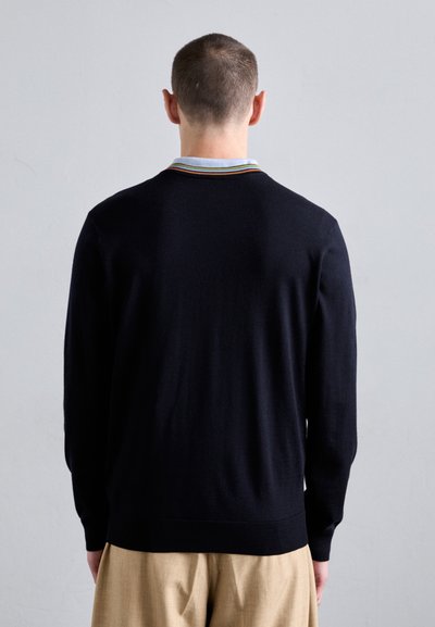 Svart strikket cardigan med rund krage, prydet med flerfargede striper. Lange ermer og ribbestrikkede mansjetter, bakfra vist.