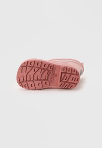 Suela de zapato de goma rosa con patrón de tracción multidireccional y detalle prominente del logo de la marca. Bisel superior liso con acentos en gris claro.