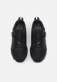 Black athletic shoes featuring a mesh upper, circular dial for tightening, and textured soles. Includes accents in dark blue on sides.