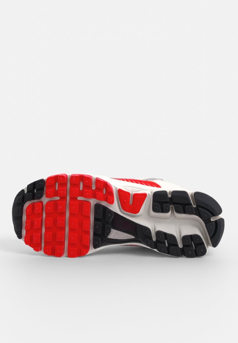 Semelle de chaussure de course avec traction en caoutchouc, affichant un mélange de couleurs noir, rouge et blanc ; design texturé avec des motifs hexagonaux et rectangulaires.
