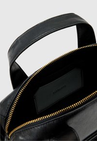 Wnętrze czarnej skórzanej torby z zamknięciem na zamek błyskawiczny w złotym odcieniu. Zawiera czarny skórzany uchwyt na karty oraz materiałową podszewkę.