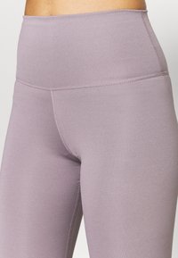 Leggings a vita alta in morbido tessuto lavanda, con una texture liscia, caratterizzati da cuciture a macchina e un design aderente.