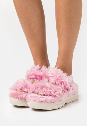Furry pink sandals with a soft texture, featuring a wide strap design and a white, cushioned sole for comfort.