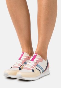 Baskets roses et crème avec des accents bleu marine, présentant une tige texturée, une fermeture à lacets et une semelle blanche subtilement surélevée.