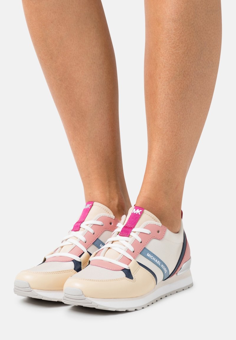 Baskets roses et crème avec des accents bleu marine, présentant une tige texturée, une fermeture à lacets et une semelle blanche subtilement surélevée.