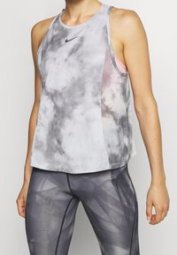 Top sportivo tie-dye grigio e bianco con scollatura rotonda, caratterizzato da un logo sottile e un design a strati. Indossato con leggings a motivo geometrico.