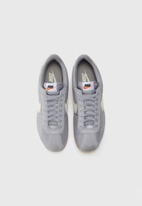 Nike-sneakers med en grå mockaöverdel, vita accenter och en traditionell snörningsdesign. Har en märkeslogotyp på tungan och en texturerad sula.