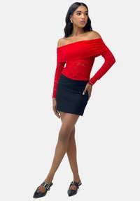 Rød blonde off-shoulder top med lange ærmer, parret med en tætsiddende sort mini nederdel og sorte spidse sko med spænde-detalje.