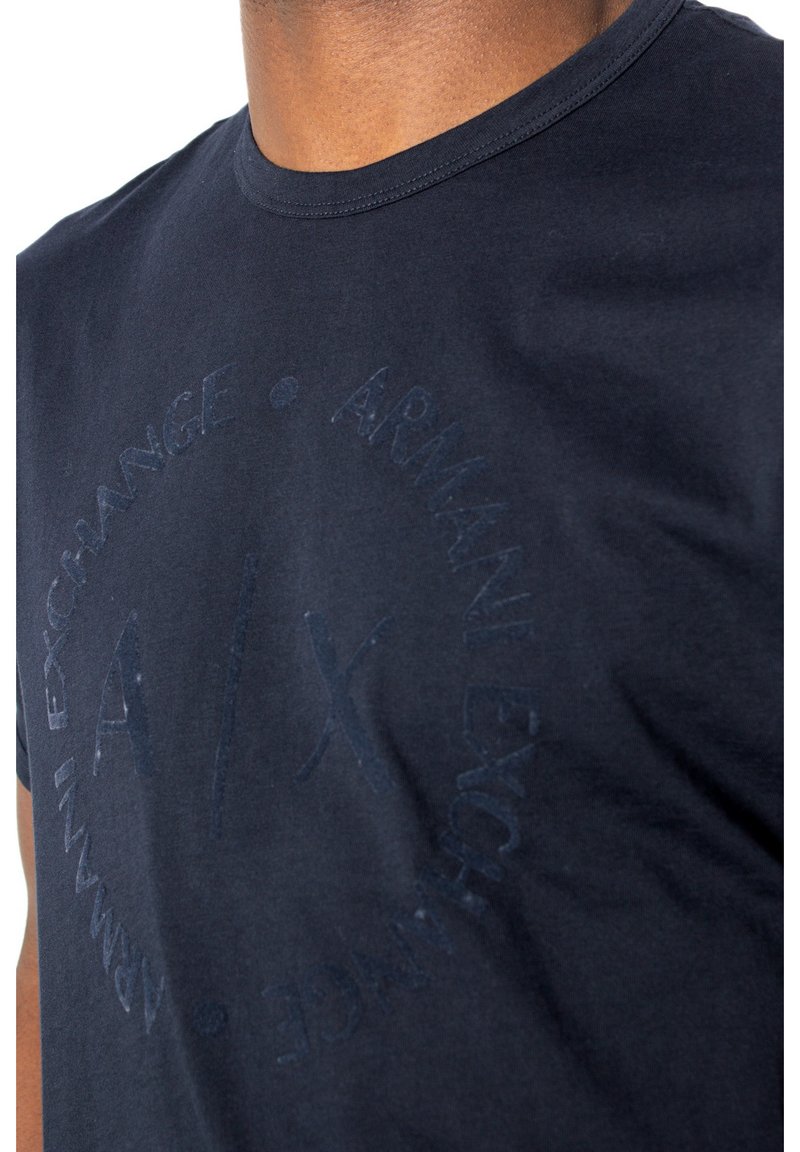 Granatowa bawełniana koszulka z tonowym logo graficznym na środku, okrągłym dekoltem i krótkimi rękawami. Gładka faktura, casualowy design.