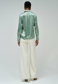 Camisa de satén verde menta con rayas, puños abotonados y un corte ajustado, combinada con pantalones anchos blancos y sandalias de tacón.