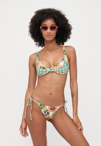 Bikini set with colorful, abstract patterns in orange, green, and blue. The top has a twist front and adjustable straps; the bottom has tie-side details.