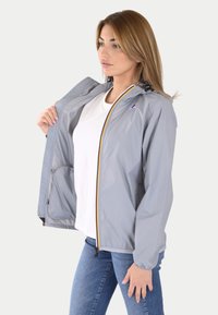 Giacca leggera grigia con chiusura a zip, strisce contrastanti gialle, blu e rosse, e polsini elastici. Dotata di cappuccio e tasca interna.