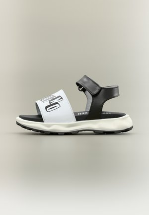 Sandalo open-toe bianco e nero con suola spessa, cinturino regolabile alla caviglia e ampia fascia frontale con testo nero audace.