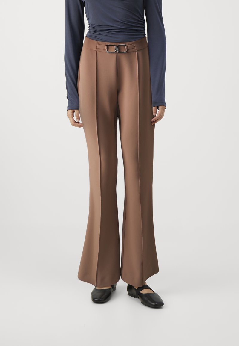 Pantalon marron taille haute à jambes larges avec ceinture à double boucle, associé à des chaussures plates noires et un haut bleu marine à manches longues.