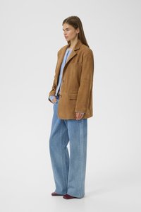 Brown suede blazer with notch lapels, two front pockets, and two buttons, paired with wide light denim jeans and burgundy shoes.