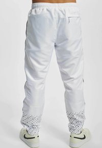 Wei�ße Jogginghose mit schwarzen Seitenstreifen, elastischem Bund, Reißverschlusstasche und gemusterten Beinabschlüssen; aus glattem, leichtem Material gefertigt.