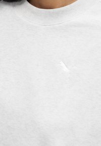 Κοντινό πλάνο λευκού πουκάμισου με στρογγυλή λαιμόκοψη και διακριτικό λευκό κεντημένο λογότυπο Puma στο αριστερό μέρος του στήθους.