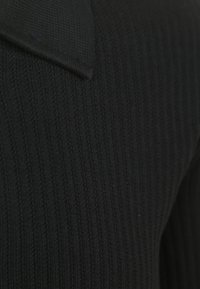 Schwarzer Strickpullover mit gerippter Textur und umgeschlagenem Kragen. Der Stoff wirkt weich und mittelschwer. Nahaufnahme, die sich auf die Materialdetails konzentriert.