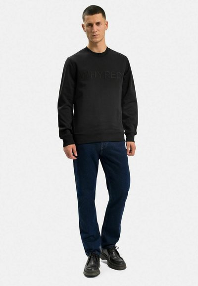 Svart sweatshirt med upphöjt "WHYRED"-logotyp på framsidan, parat med mörkblå jeans och svarta skor, med rundad halsringning och ribbade ärmslut.
