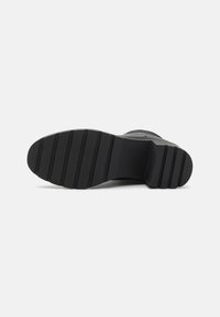 Black shoe sole with a textured surface, featuring horizontal grooves and a slightly raised heel for added grip and stability.