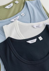 Quatre débardeurs en vert olive, bleu clair, blanc et noir, chacun avec des étiquettes « NEXT Regular Fit » et des étiquettes de taille petite visibles.