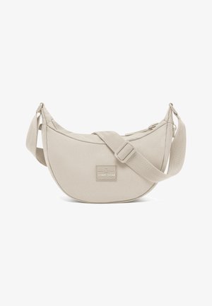 Bolso bandolera de tela beige con diseño curvado, correa ajustable y una pequeña etiqueta con el logotipo "JOHNNY URBAN". Textura suave y forma simple.