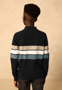 Polo de punto negro con rayas horizontales en beige, blanco y azul claro. Cuello alto y puños acanalados; ajuste informal.