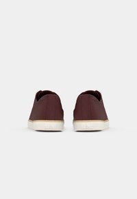 Paire de baskets marron décontractées avec semelles blanches vues de dos, montrant un design minimaliste et une coupe basse à la cheville.