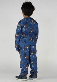 Zils sporta krekliņš un bikses ar ziemeļbrieža slidošanas izdruku, izgatavotas no mīksta auduma ar ribotām piedurknēm. Apavi ir zili ar siksnām.