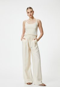 Crème kleurige tanktop met ribbelstructuur, gecombineerd met losvallende, hooggeplaatste crème broeken met een elastische tailleband en zijzakken.