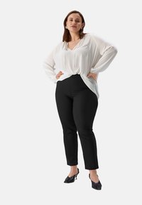 Witte blouse met lange mouwen en een losse pasvorm, gecombineerd met zwarte slim-fit broek. De outfit heeft een gladde textuur en minimale ontwerpdetails.