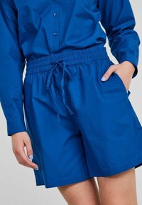 Siniset shortsit kevyestä kankaasta, joissa on elastinen vyötärönauha ja kiristysnyöri, sivutaskut ja löysä istuvuus.