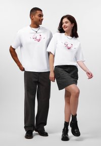 Hvide T-shirts med korte ærmer, der har et pink grafisk design; parret med mørke bukser og en grå cargo-nederdel. Sorte ankelstøvler fuldender looket.